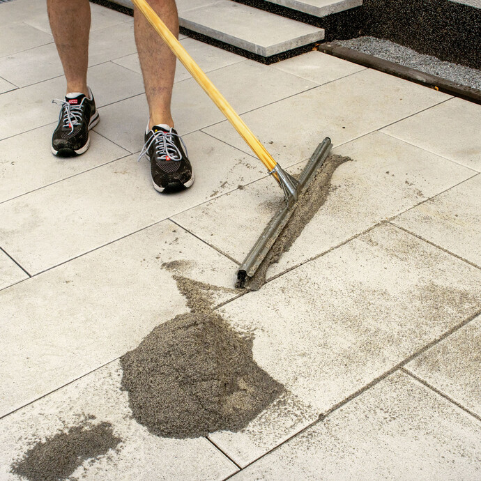 Pflasterfugenmörtel Fix mit feinem Wasserstrahl und Gummischieber in die Fugen der Terrassenplatten einbringen.